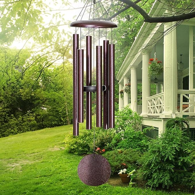 Memorial wind chime with bronze tubes hanging in a sunlit garden beside a white porch